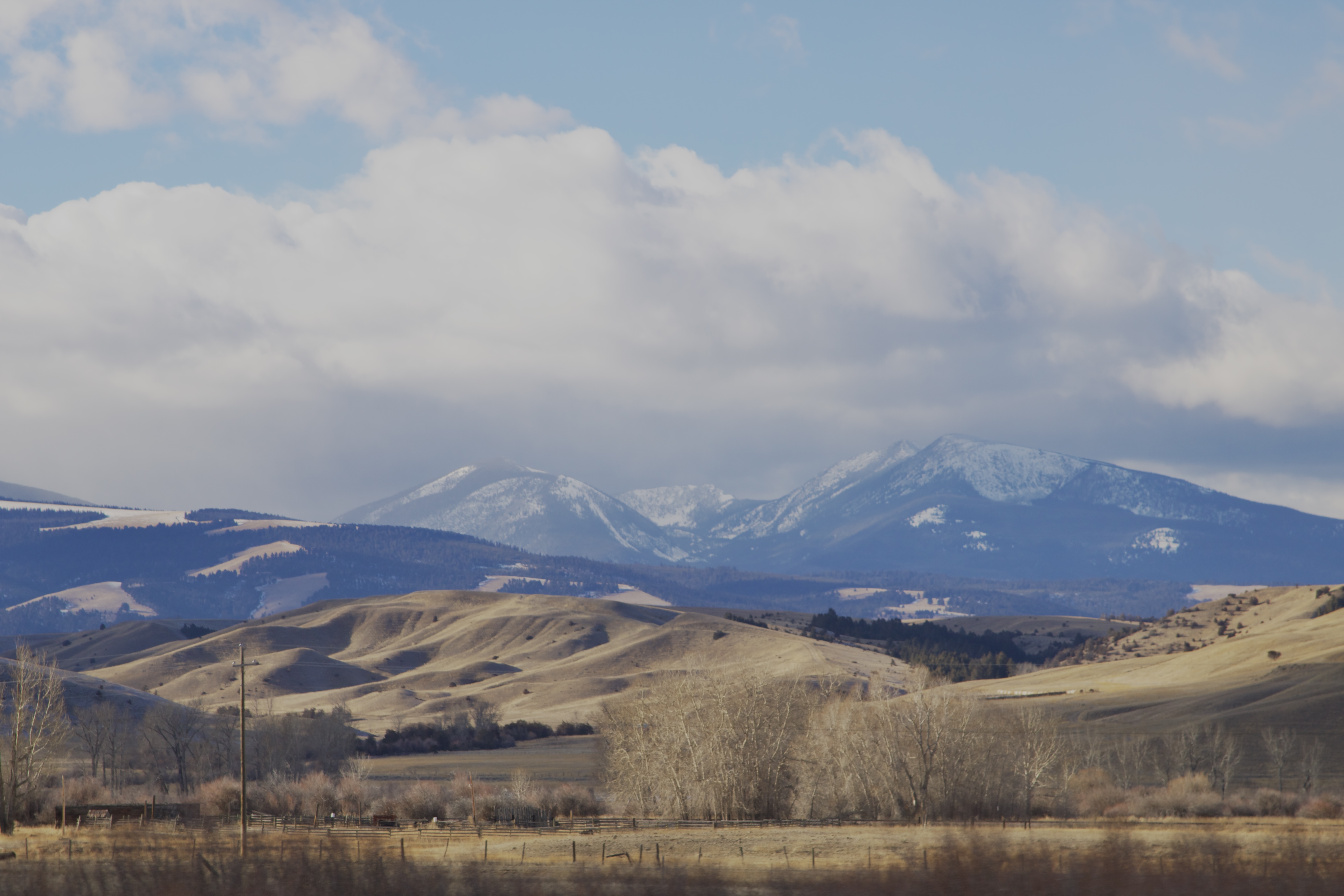 A snowy mountain in the distance, covered with fog. The land in front of it is dry and dusty rolling hills